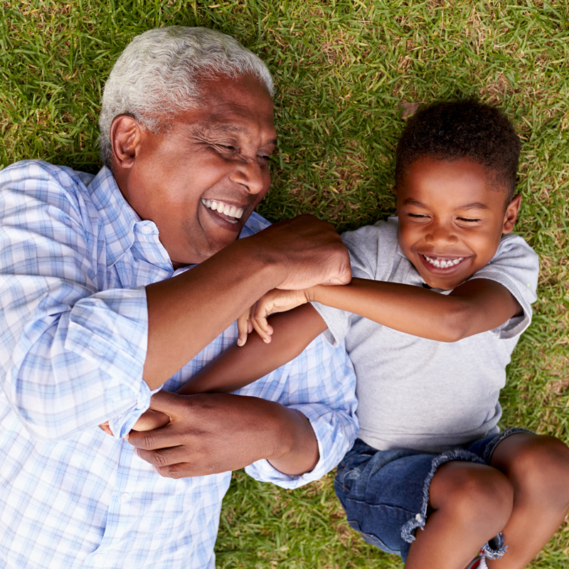 Grandfather and Grandson Lay on Grass Laughing